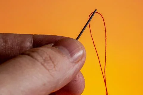 Needle in hand with a red thread on a Lush Lava background. close up copy space Foto stock