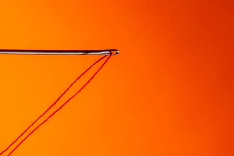 A needle hanging on a red thread on a Lush Lava background. close up copy space Foto stock