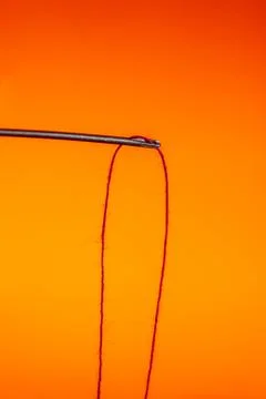 A needle hanging on a red thread on a Lush Lava background. close up copy space Stock Photos
