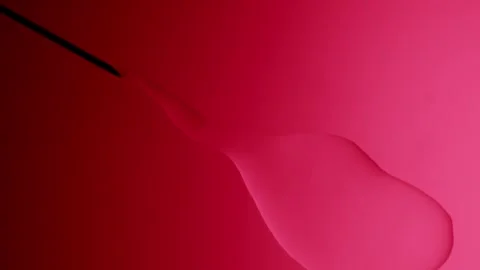 Needle injects liquid on a red gradient background 動画素材 303060381