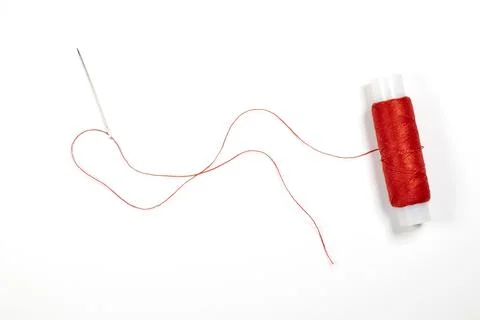 Needle with red thread and spool of thread on a white background Stock Photos