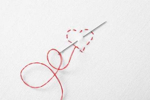Needle with red thread and stitches in shape of heart on white fabric, top vi Stock Photos