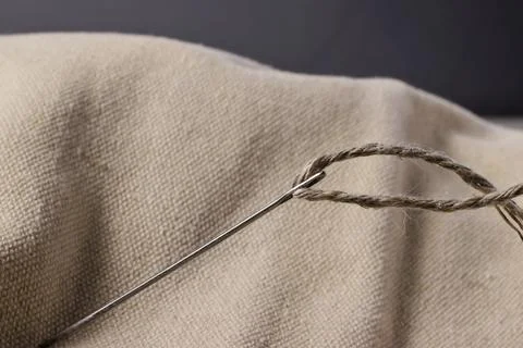 A needle with a thick thread is stuck into rough fabric. Stock Photos
