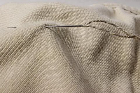 A needle with a thick thread is stuck into rough fabric. Foto stock