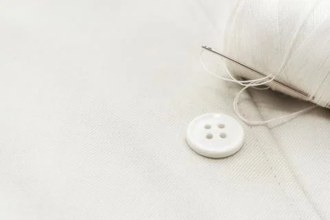 Needle with white threads, buttons on white fabric, clothes. Part of men's cl Stock Photos