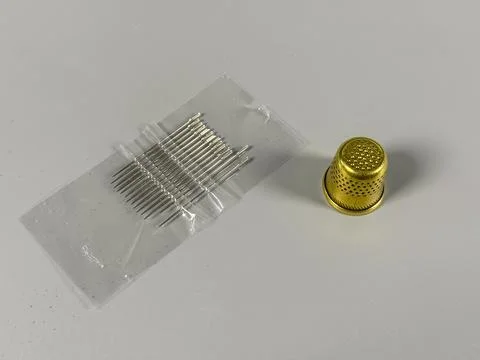 Needles and thimble placed on a plain surface for sewing tasks Stock Photos