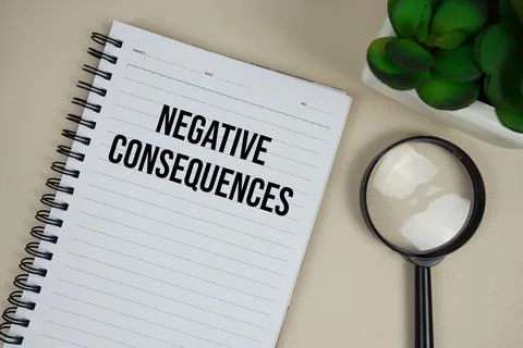 Negative Consequences text on paper notebook with magnifying glass on beige.. Stock Photos