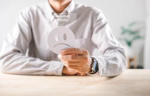 Negative customer feedback clearly shown as hand holds sad face icon, sugge.. Stock Photos