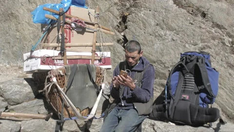 Nepali porter with load at choosing music he will listen to on the way to Namche Stock Footage 236912341