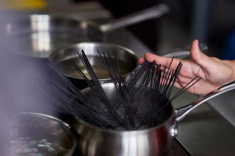 Nera pasta is manually dipped in a pot of boiling water in the kitchen Stock Photos