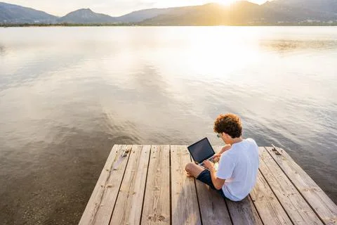 Nerd guy spending time outdoor programming at sunset writing code using lapto 写真素材