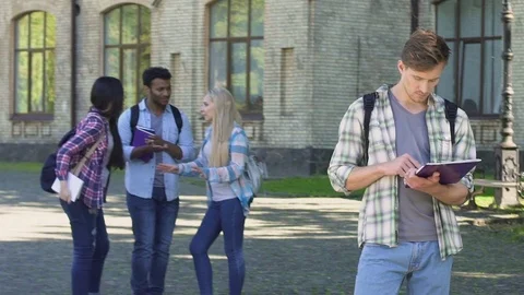 Nerd male standing alone and reading essay, group of multiracial friends talking Stock Footage