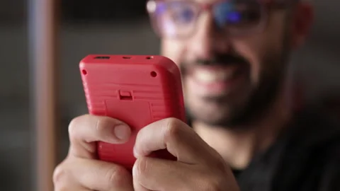 Nerd plays with a little red retro video game. Male game player. Portrait shot Stock Footage 136973596