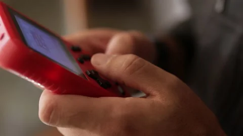 Nerd plays with a little red retro video game. Male game player. Hands close up Video stock 136973883