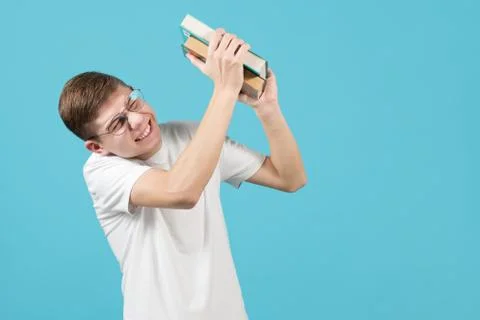 The nerd squints and as if trying to protect himself, keeps books aside Stock Photos