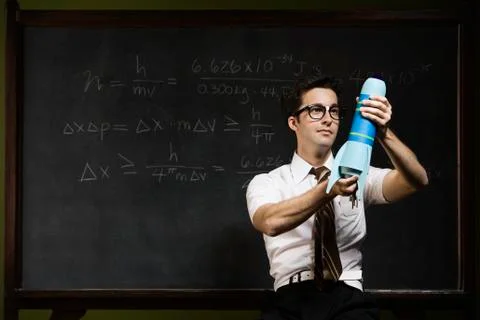 Nerdy man holding rocket model in front of blackboard Foto stock