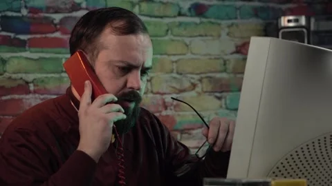 Nervous IT Guy Having Argument Over Landline Telephone in Front of Desktop Stock Footage 306366694