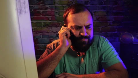 Nervous Man Having Call Over Old Mobile Phone in Front of Desktop Computer Video stock 302473429