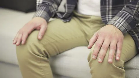 Nervous man sitting on sofa while holding hands on knees. Slow motion Stock Photos