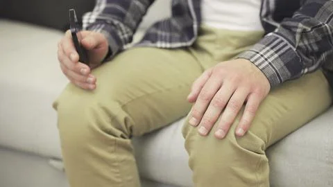 Nervous man sitting on the sofa while using mobile phone and typing message Fotos de archivo