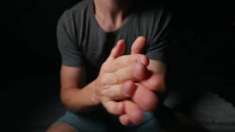 Nervous Young Man Rubbing His Hands Together in Moody Dark Room Setting Stock Footage 339366231