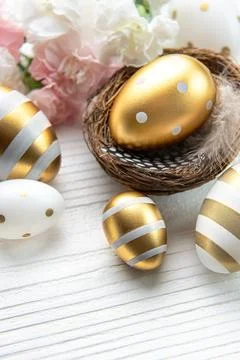 Nest with Easter eggs painted golden colors on a white wooden background. Stock Photos