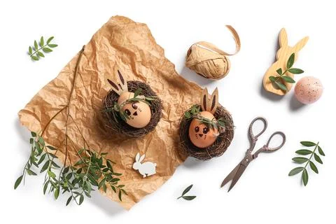 Nests of cute painted Easter eggs with drawn face, supplies and leaves on whi Stock Photos