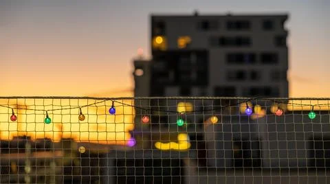 Net fence with festive multicolored string lights draped across it in the evenin Foto stock