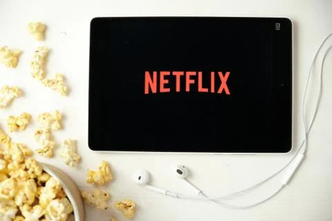 Netflix logo on the screen of the tablet laying on the white table and sprinkled Illustrazione stock