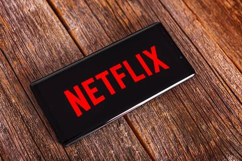 The Netflix program is open on a black smartphone lying on a wooden table. 스톡 사진