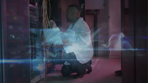 Network technician kneeling typing on laptop routing cables for connectivity, Stock Footage 313328144