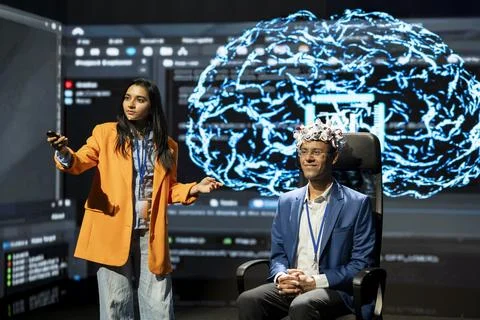 Neuroscientist presenting AI brain data next to EEG participant Stock Photos