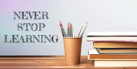 Never stop learning. A pencil holder with pencils sits on a table with a stack Stock Photos