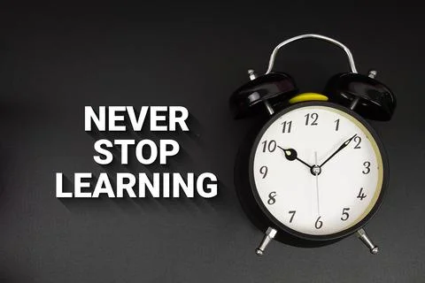 Never Stop Learning text with alarm clock on black background Stock Photos