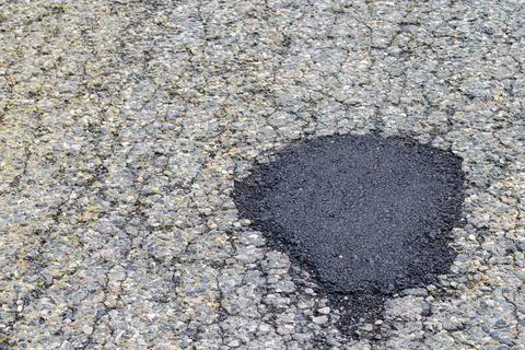 New asphalt patch laid on repaired road. Old asphalt road pothole pit. Fresh  Stock Photos