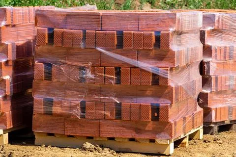 New bricks packed in a pallet standing on a clay surface of a construction site Stock Photos