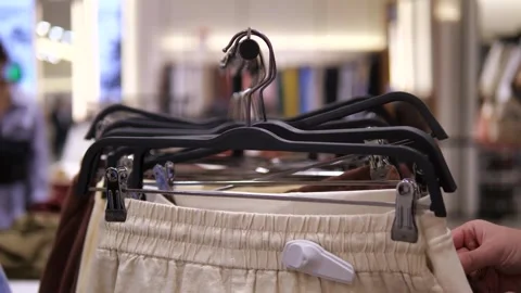 New light pants or shorts hanging on hangers in a store and womens hands Stock Footage 313271053