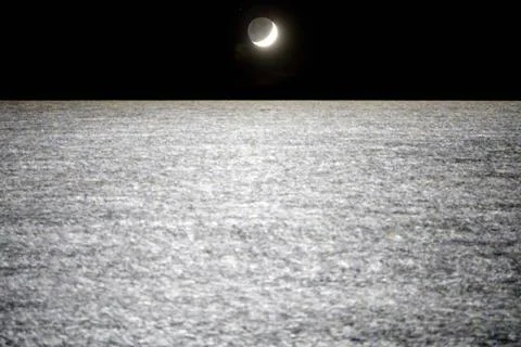 New moon setting over the sea. Crescent moon setting over empty sea at night. Stock Photos
