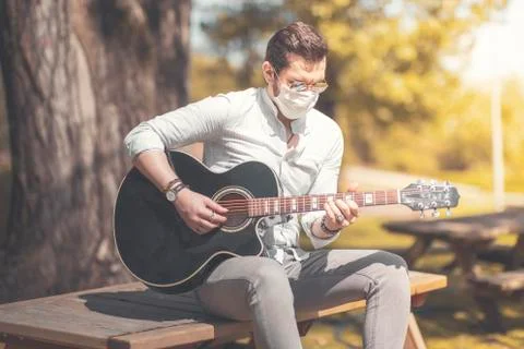 New normal concept, a young man with a mask is playing a guitar at outside wi 스톡 사진