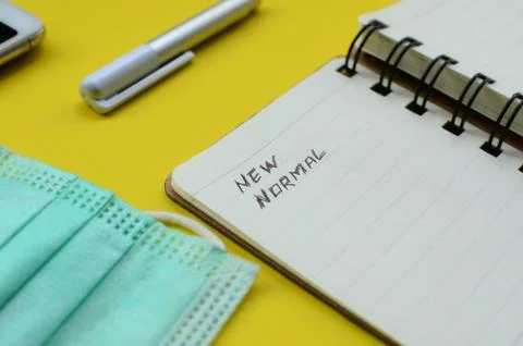 New Normal text on note pad with face mask ,cell phone, and pen on yellow backgr Stock Photos