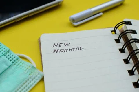 New Normal text on note pad with face mask ,cell phone, and pen on yellow backgr Stock Photos