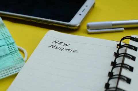New Normal text on note pad with face mask ,cell phone, and pen on yellow backgr Stock Photos