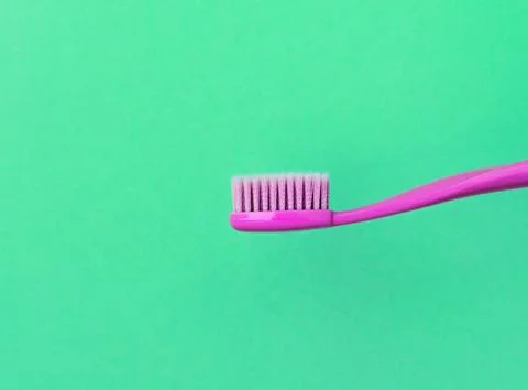 New pink toothbrush without toothpaste on green background. Close up side view. Stock Photos