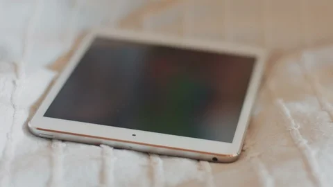 New silver digital tablet lying on bed. Two girls taking tablet in hands. Happy Stock-Footage 85630992