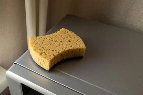 New sponge with black abrasive side on a grey microwave oven. kitchen cleaning Stock Photos