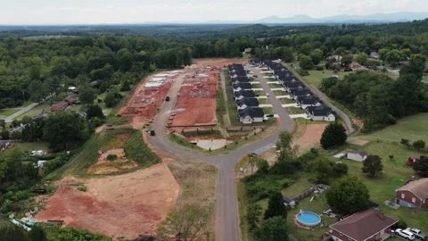 A new subdivision of black roofed homes rises on graded red clay beside older Stock Footage 345684172