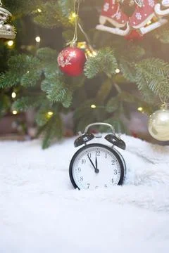 New Year's clock with an alarm clock on a background decorated with lights. Stock Photos