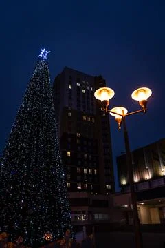 New Year's tree on the background of a multi-storey building and a street lam Stock Photos
