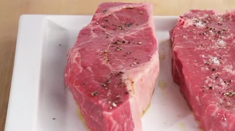 New York strip steaks being seasoned with salt Stock Footage 24656777