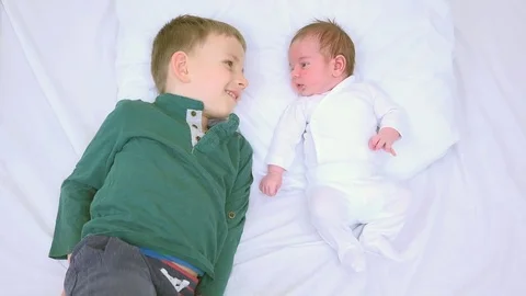 Newborn and bigger brother lying on bed looking to each other, building relation Stock Footage